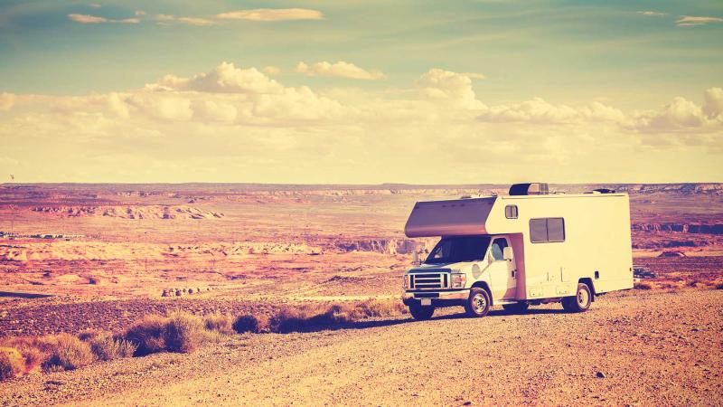 An RV parked on a dirt road with open sky and desert in the background.