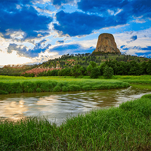 A scenic landscape with a river and clouds overlooking Devils Tower.