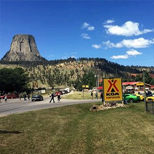 People and parked cars at the Devils Tower KOA campsite and Devils Tower National Monument in the background.