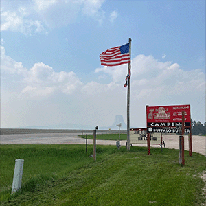 A raised flag beside a sign on a grassy area at Devils Tower View Campground.