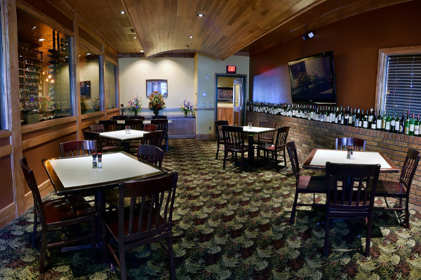 Tables and wooden chairs fill the patterned floor, showcasing an array of wine bottles across the space of The Prime Rib Restaurant & Wine Cellar.