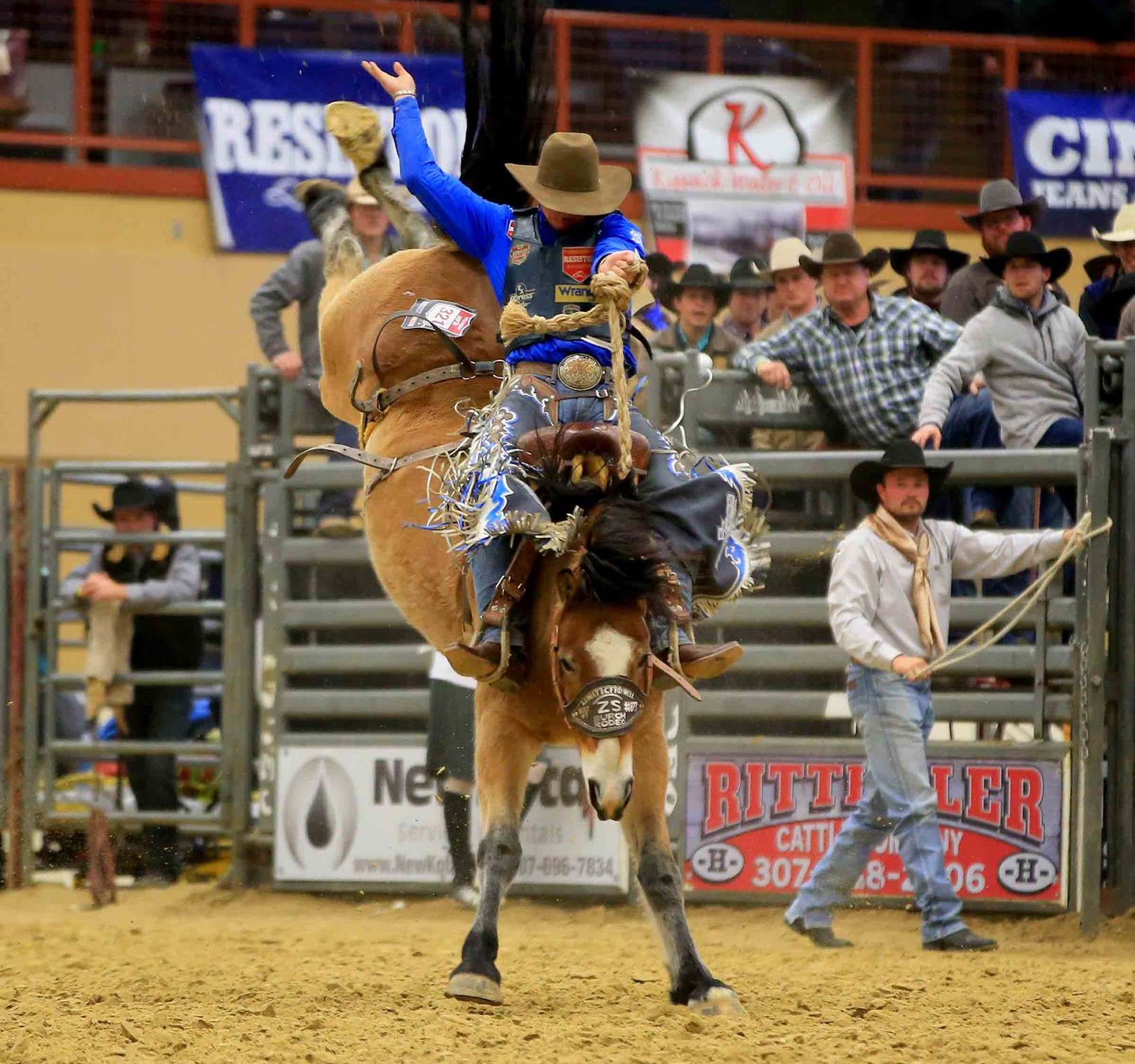 A man riding a bucking bronco in an indoor rodeo arena in Wyoming, filled with spectators at the New Year’s Eve Buck & Ball in Campbell County.